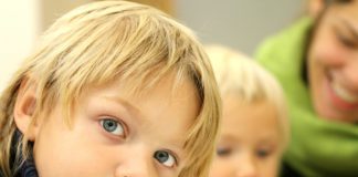 A young boy in a classroom looking up at camera.