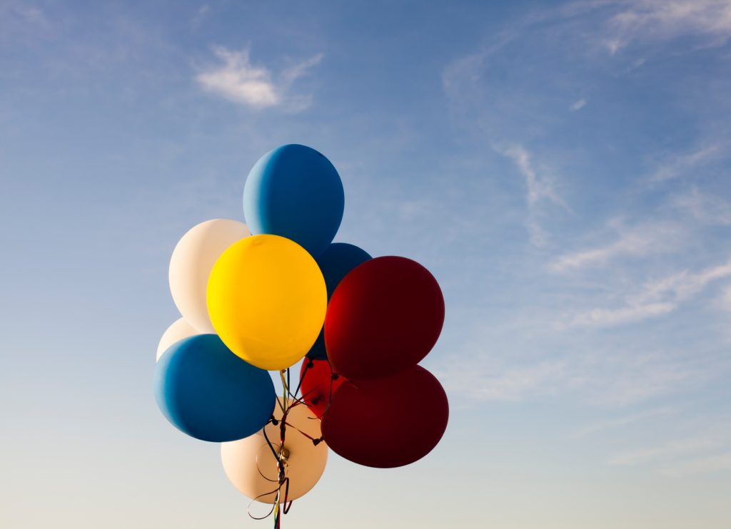 A bundle of multi-coloured balloons against a background of blue sky.