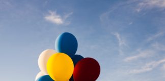 A bundle of multi-coloured balloons against a background of blue sky.