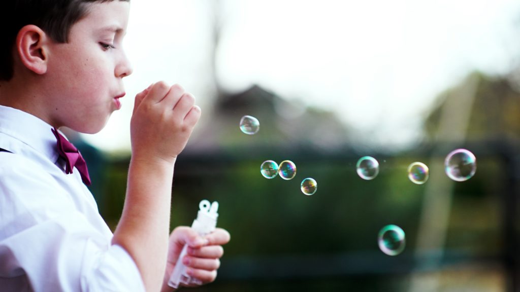 A young boy wearing a bow tie blowing bubbles.