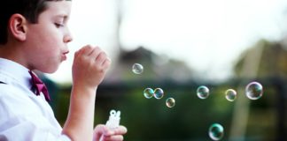 A young boy wearing a bow tie blowing bubbles.