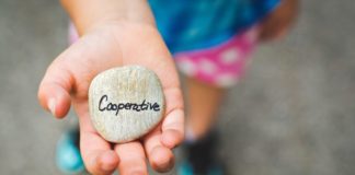 A young girl holding a stone in her hand that has the word "co-operative" written on it.