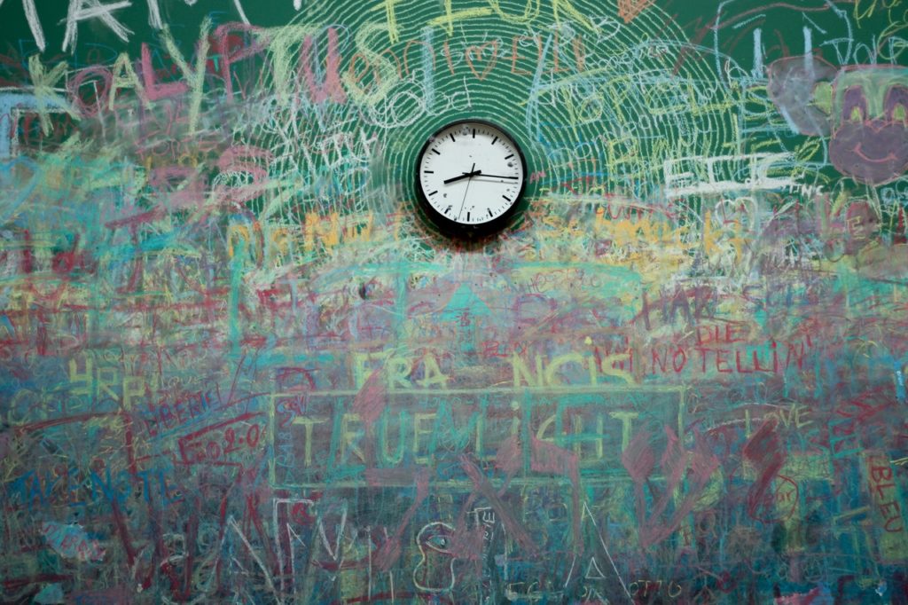 A clock on a green wall covered in graffiti