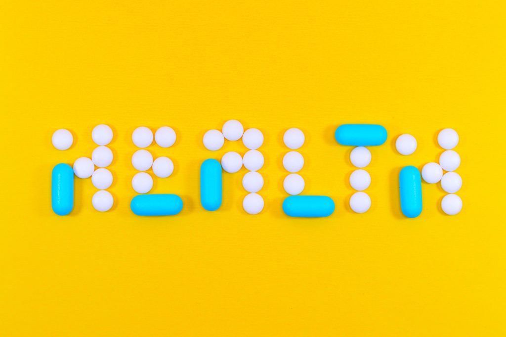 Pills arranged to spell out 'health' against a bright yellow background.