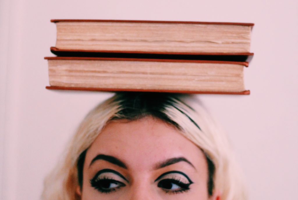 A woman balancing two books on her head against a pink background