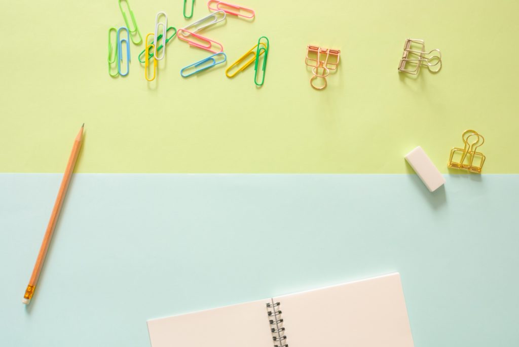 A blank notebook against a blue and yellow background surrounded by coloured paperclips.