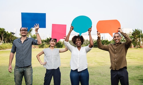 Four people holding up speech bubbles in a field.