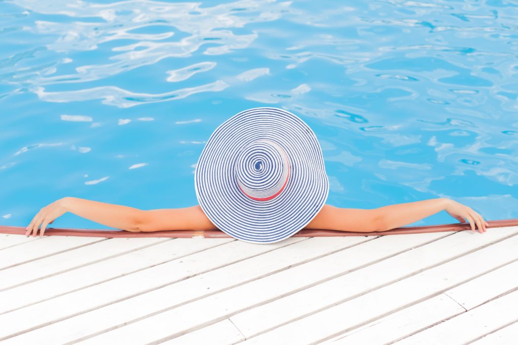 Teachers summer holidays. A woman wearing a sun hart relaxing in a pool.