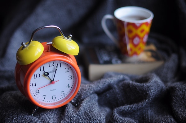 An orange alarm clock on a blanket next to an orange mug.