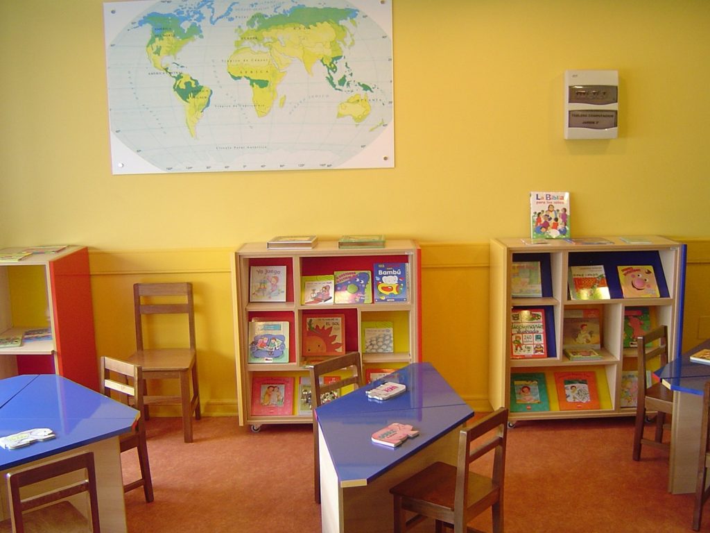 A classroom with yellow walls and blue tables and bookshelves.