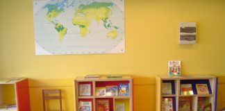 A classroom with yellow walls and blue tables and bookshelves.