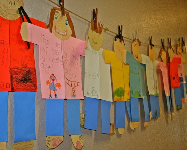 A row of colourful paper people hanging on a wall.